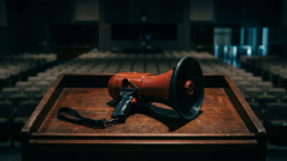 A red and black bullhorn megaphone resting on a dark wooden podium in an empty auditorium.
